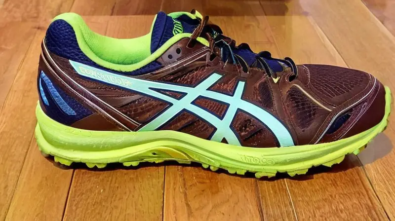 Los zapatos Asics Speed Trail Fuji están ubicados en un suelo de madera con una coloración marrón oscuro en la parte inferior y detalles deportivos