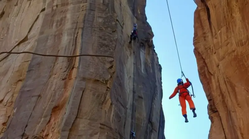 En un paisaje montañoso, una figura en trajes brillantes de seguridad se sujeta con una amarre al lado de una cuerda fija mientras el sistema de poleas de metal asciende por la pared rocosa