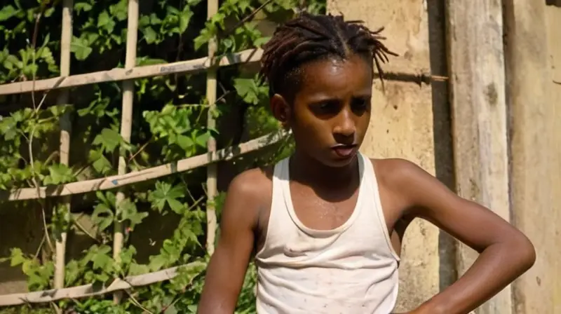 Un niño pobre con una apariencia desnutrida se sienta en medio de un entorno severo, rodeado de estructuras endurecidas y vegetación salvaje